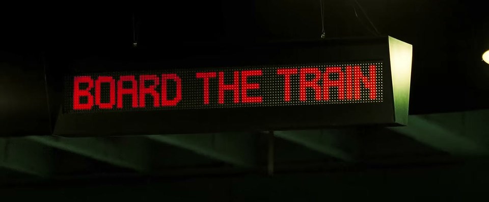 04_board_train.jpg — 역 전광판에 뜬 "BOARD THE TRAIN" (영화 『이글 아이』 장면)